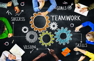 people sitting at a table working with images of gears and the words Success, Goals, Teamwork, and Skills drawn on the table