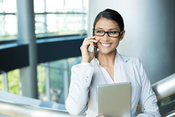a woman smiling while on the phone and holding a notebook